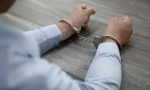 Ręce w kajdankach, symbolizujące konsekwencje udziału w zorganizowanej grupie przestępczej.