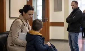Rodzina w sądzie, matka z synem siedzą, ojciec stoi z boku. Sytuacja sugeruje wniosek o ustalenie kontaktów z dzieckiem.