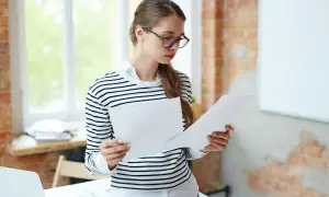 Młoda kobieta w okularach analizuje dokumenty, być może dotyczące ustalenia stosunku pracy.