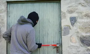 Osoba w masce próbuje wyważyć drzwi łomem. To próba kradzieży z włamaniem.
