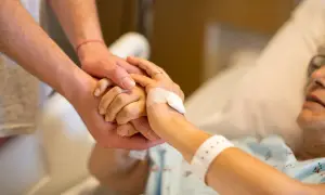 Dłoń opiekuna obejmuje dłoń osoby starszej w łóżku. Po śmierci osoby ubezwłasnowolnionej opiekun prawny ma obowiązki.