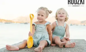 Dwie uśmiechnięte dziewczynki, przyrodnie rodzeństwo, bawią się na plaży z żółtą łopatką.