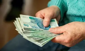 Dłonie trzymające polskie banknoty, być może jako dodatek za pracę w warunkach szkodliwych. Widoczne nominały 50 i 100 zł.