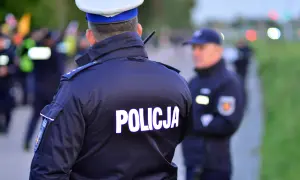 Policjant w mundurze z napisem "POLICJA" na plecach. Czy policjant może mnie przeszukać na ulicy? W tle inni funkcjonariusze i niewyraźne sylwetki.