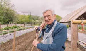 Uśmiechnięty starszy pan z narzędziem w ręku, pracujący w ogrodzie. Jego staż pracy w gospodarstwie rolnym od 16 roku życia to jego duma, a dokumenty potwierdzają lata doświadczenia.