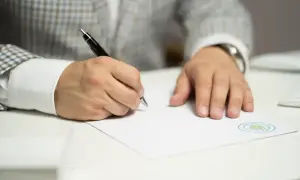 Mężczyzna w eleganckim garniturze pisze długopisem na białej kartce, przygotowując uzasadnienie pozwu o alimenty.