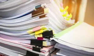 Stosy dokumentów, w tym potencjalny duplikat świadectwa pracy, z kolorowymi spinaczami i zakładkami.