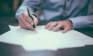 Dłoń pisze na dokumencie, co może być związane z fałszowaniem dokumentów i wyrokami sądowymi.