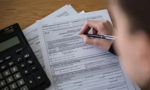 Ręka wypełnia PIT-37, obok leży kalkulator. Rozliczenie podatkowe w Polsce.