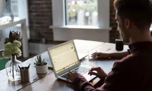 Mężczyzna pracuje na laptopie, nawet w sobotę. W tle widać okno i kwiaty.