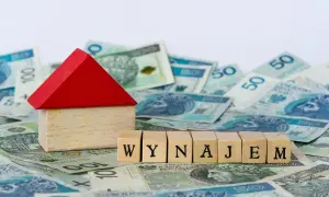 Drewniany domek i kostki z napisem "WYNAJEM" na tle polskich banknotów. Zastanawiasz się nad najmem okazjonalnym i podatkiem?
