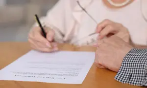 Kto ma wgląd do testamentu? Dłoń podpisuje dokument "Last Will and Testament", a obok spoczywa druga dłoń.