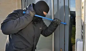 Mężczyzna w kominiarce i rękawiczkach próbuje wyważyć drzwi łomem. To próba kradzieży z włamaniem.