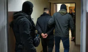 Funkcjonariusze zatrzymują podejrzanego, który jest częścią zorganizowanej grupy przestępczej. Mężczyzna ma założone kajdanki.