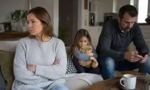 Smutna dziewczynka tuli misia, podczas gdy rodzice siedzą obok siebie, ale w ciszy. Tak wygląda życie w separacji.