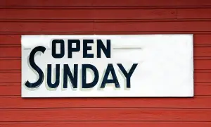 Tablica "OPEN SUNDAY" na czerwonej, drewnianej ścianie. To znak, że praca w niedziele jest możliwa.