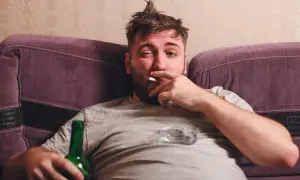 Mężczyzna z papierosem i butelką piwa na kanapie. Ciężki obowiązek alimentacyjny wobec brata alkoholika.