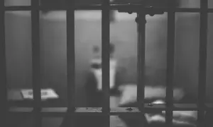 Widok przez kraty więzienne. Rozmazana postać w tle sugeruje nadzieję na odroczenie kary pozbawienia wolności.