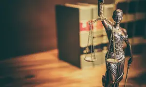 Figurka Temidy z wagą symbolizuje sprawiedliwość. W tle widać regały z książkami, sugerujące prawniczy kontekst, jak wniosek o wstrzymanie wykonania kary do czasu rozpatrzenia wniosku wzór.