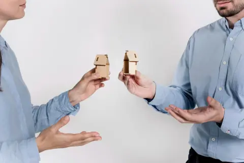 Rozdzielność majątkowa a wspólny dom: dwoje ludzi trzyma miniaturowe domki, symbolizujące podział majątku.