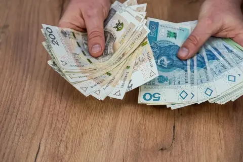 Dłonie trzymają stos banknotów 200 zł i 50 zł. Może to być wypłata pieniędzy przed śmiercią, jako testament.