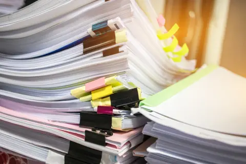 Stosy dokumentów, w tym potencjalny duplikat świadectwa pracy, z kolorowymi spinaczami i zakładkami.