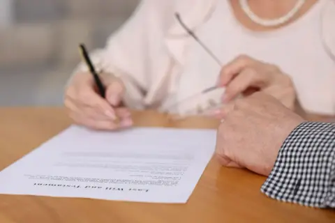 Kto ma wgląd do testamentu? Dłoń podpisuje dokument "Last Will and Testament", a obok spoczywa druga dłoń.