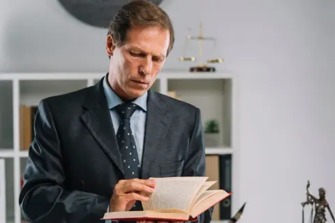 Prawnik w garniturze studiuje kodeks karny paragrafy, szukając odpowiedzi w księdze.