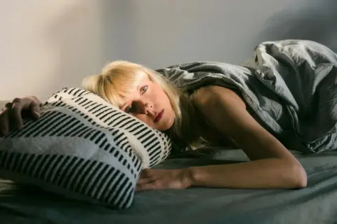 Kobieta leży w łóżku, przytulając poduszkę. Może to być obraz symbolizujący potrzebę urlopu menstruacyjnego w Polsce.