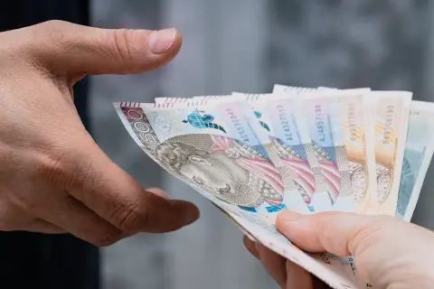 Dwie dłonie przekazują sobie plik banknotów. Zastanawiasz się, ile bank zabiera po śmierci?
