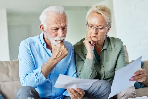 Zamyśleni seniorzy analizują dokumenty, szukając informacji, jak zapisać mieszkanie w testamencie wzór.
