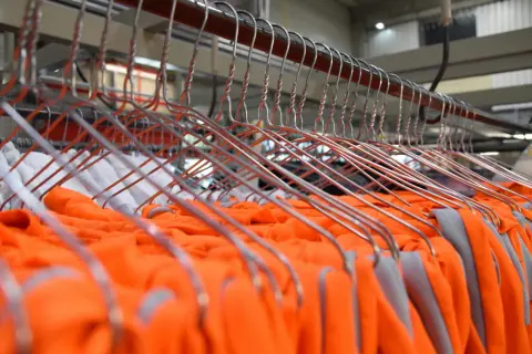 Pomarańczowe i białe ubrania wiszą na wieszakach, gotowe do odbioru. To ekwiwalent za pranie, który zapewnia świeżość i porządek.