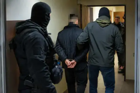 Funkcjonariusze zatrzymują podejrzanego, który jest częścią zorganizowanej grupy przestępczej. Mężczyzna ma założone kajdanki.