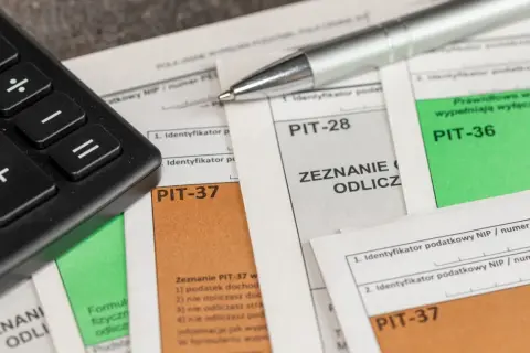 Kalkulator i długopis leżą na dokumentach PIT-37, PIT-28 i PIT-36. Czas na rozliczenie podatku i skorzystanie z ulg, czyli ikze odliczenie od podatku.