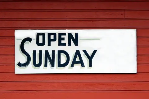 Tablica "OPEN SUNDAY" na czerwonej, drewnianej ścianie. To znak, że praca w niedziele jest możliwa.