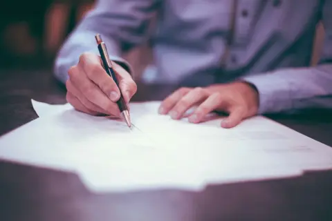 Ręka pisze na dokumencie, zastanawiając się, jaki podatek od spadku po wujku będzie należny.