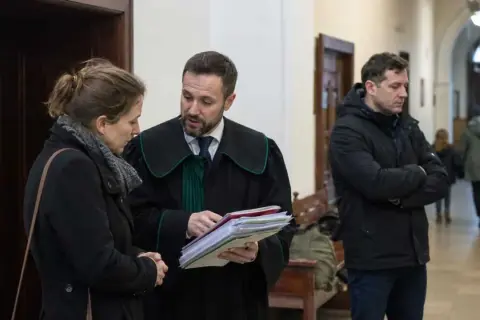 Prawnik w todze omawia dokumenty z kobietą, podczas gdy mężczyzna w kurtce czeka. Sprawa dotyczy artykułu 109 KRIO.