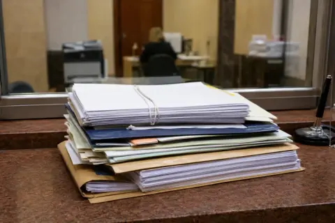 Stos dokumentów do sprawy spadkowej w sądzie, gotowy do złożenia. Obok długopis na łańcuszku.