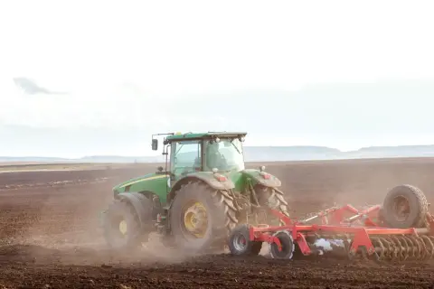 Zielony traktor orze pole. To obraz przyszłości, gdzie przekazanie gospodarstwa rolnego idzie w parze z opieką nad rodzicami, zapewniając stabilność i ciągłość.