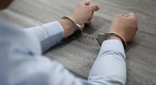 Ręce w kajdankach, symbolizujące konsekwencje udziału w zorganizowanej grupie przestępczej.