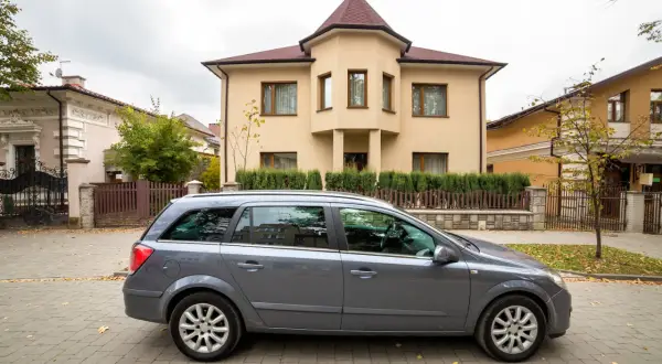 Szary kombi przed domem, symbol dziedziczenia samochodu po ojcu. Jesienne liście na bruku.