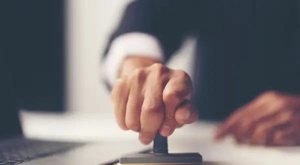 Dłoń z pieczątką, symbolizująca finalizację formalności po uzyskaniu aktu poświadczenia dziedziczenia. Co dalej?