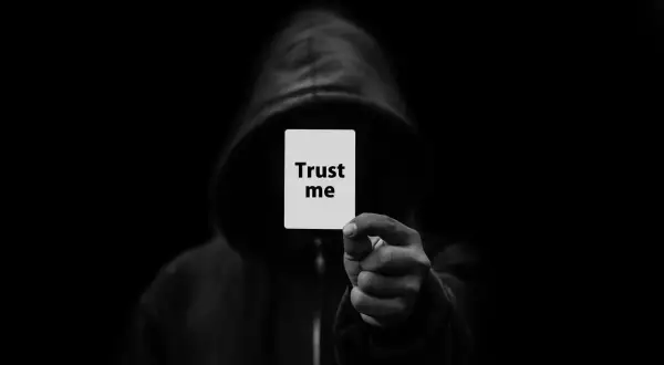 Postać w kapturze trzyma kartkę z napisem "Trust me". To symbol oszustwa, które może być karane z kodeksu karnego.