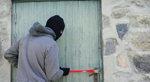 Osoba w masce próbuje wyważyć drzwi łomem. To próba kradzieży z włamaniem.