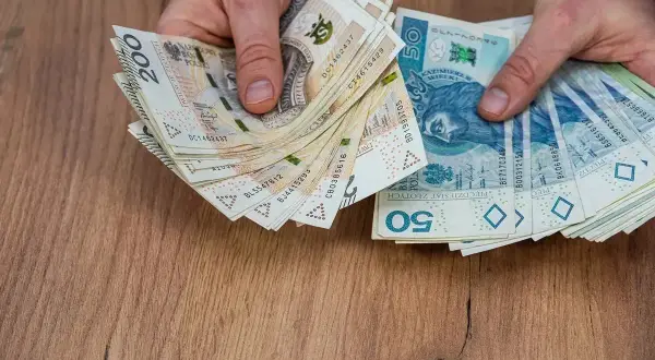 Dłonie trzymają stos banknotów 200 zł i 50 zł. Może to być wypłata pieniędzy przed śmiercią, jako testament.