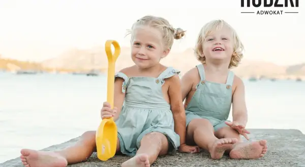 Dwie uśmiechnięte dziewczynki, przyrodnie rodzeństwo, bawią się na plaży z żółtą łopatką.