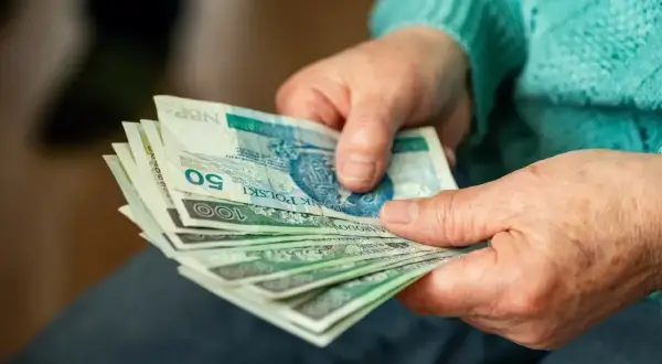 Dłonie trzymające polskie banknoty, być może jako dodatek za pracę w warunkach szkodliwych. Widoczne nominały 50 i 100 zł.