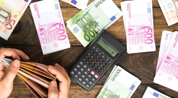 Ręce liczą banknoty euro. Obok kalkulator i stosy pieniędzy. Planowanie spadku dla obcej osoby i podatek od niego.