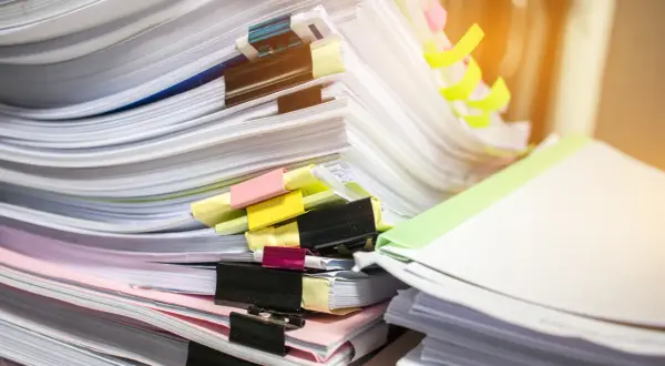 Stosy dokumentów, w tym potencjalny duplikat świadectwa pracy, z kolorowymi spinaczami i zakładkami.