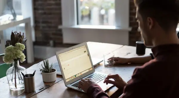 Mężczyzna pracuje na laptopie, nawet w sobotę. W tle widać okno i kwiaty.